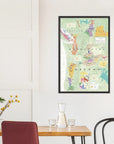The De Long Wine Map of the Pacific Northwest Framed hangs above a dining table with chairs and a vase on a white wall.