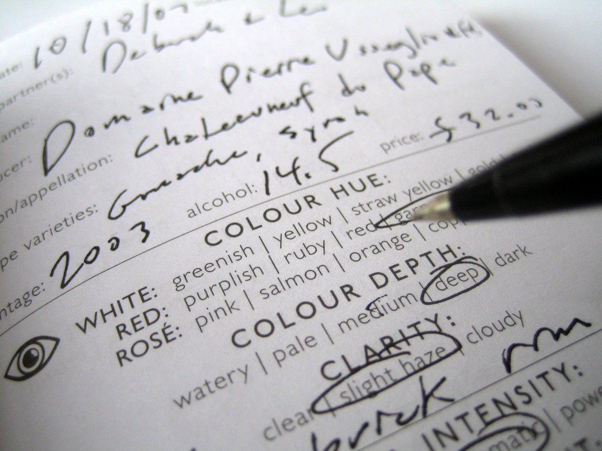 A close-up of a wine tasting notes sheet, filled in by hand, with a pen pointing to the word deep in the COLOUR DEPTH section. Various sections about the wine are visible.