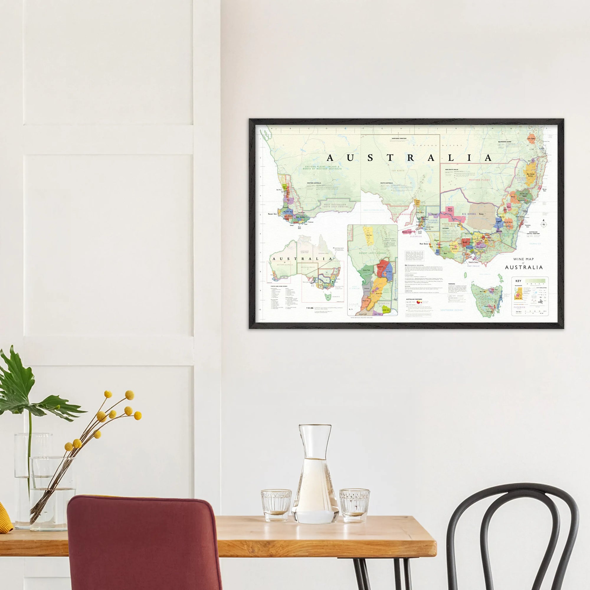 The De Long Wine Map of Australia Framed hangs on a white wall above a dining table with chairs and a glass carafe.