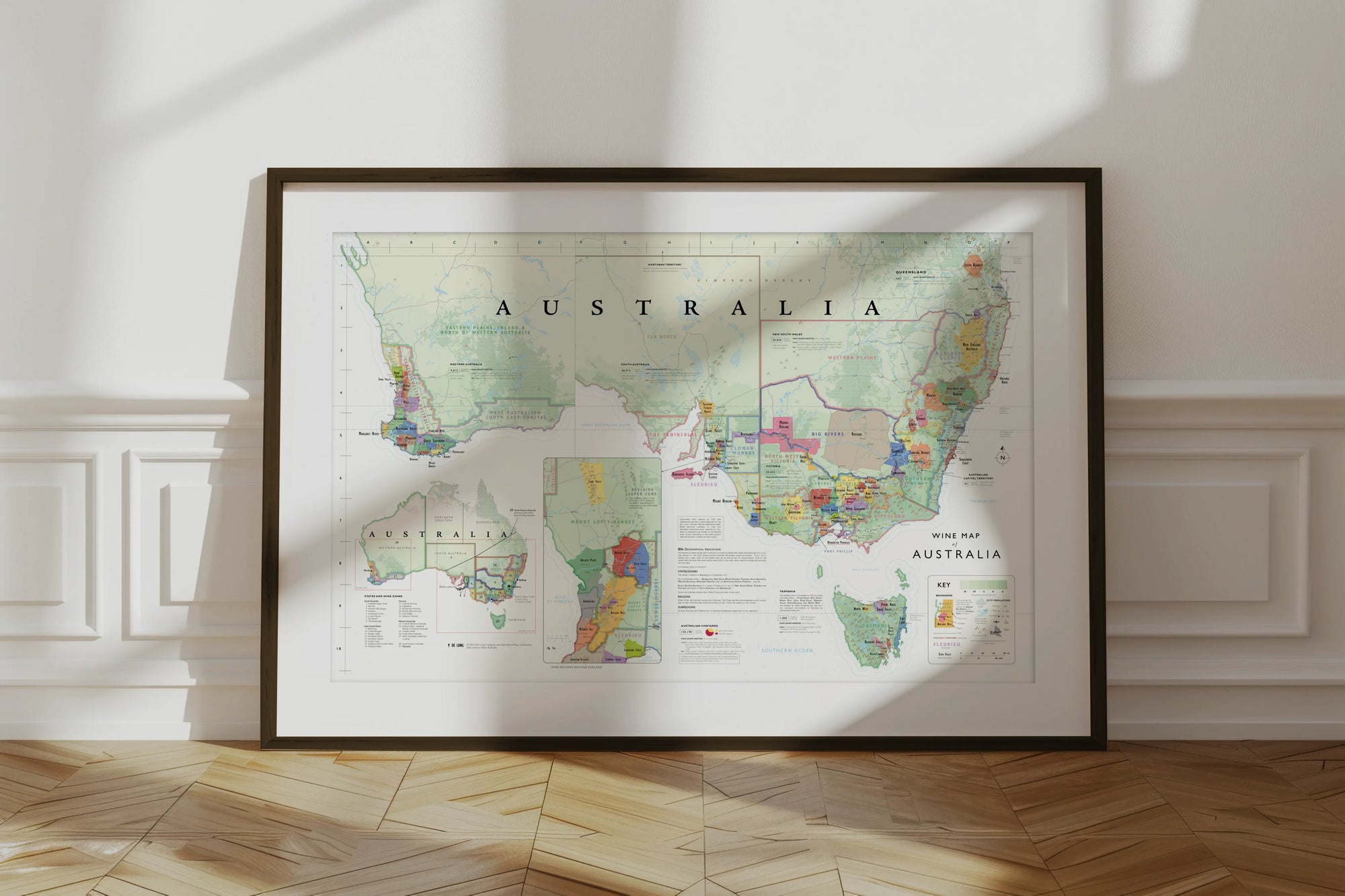 The De Long Wine Map of Australia Framed leans against a white wall, sunlight casting shadows on the wooden floor.