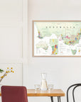 A De Long Wine Map of Australia Framed hangs on a white wall above a dining table with chairs and a glass carafe.