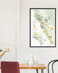 De Long Wine Map of California Framed (24x36") showcased above a dining table with chairs, glassware, and a plant.