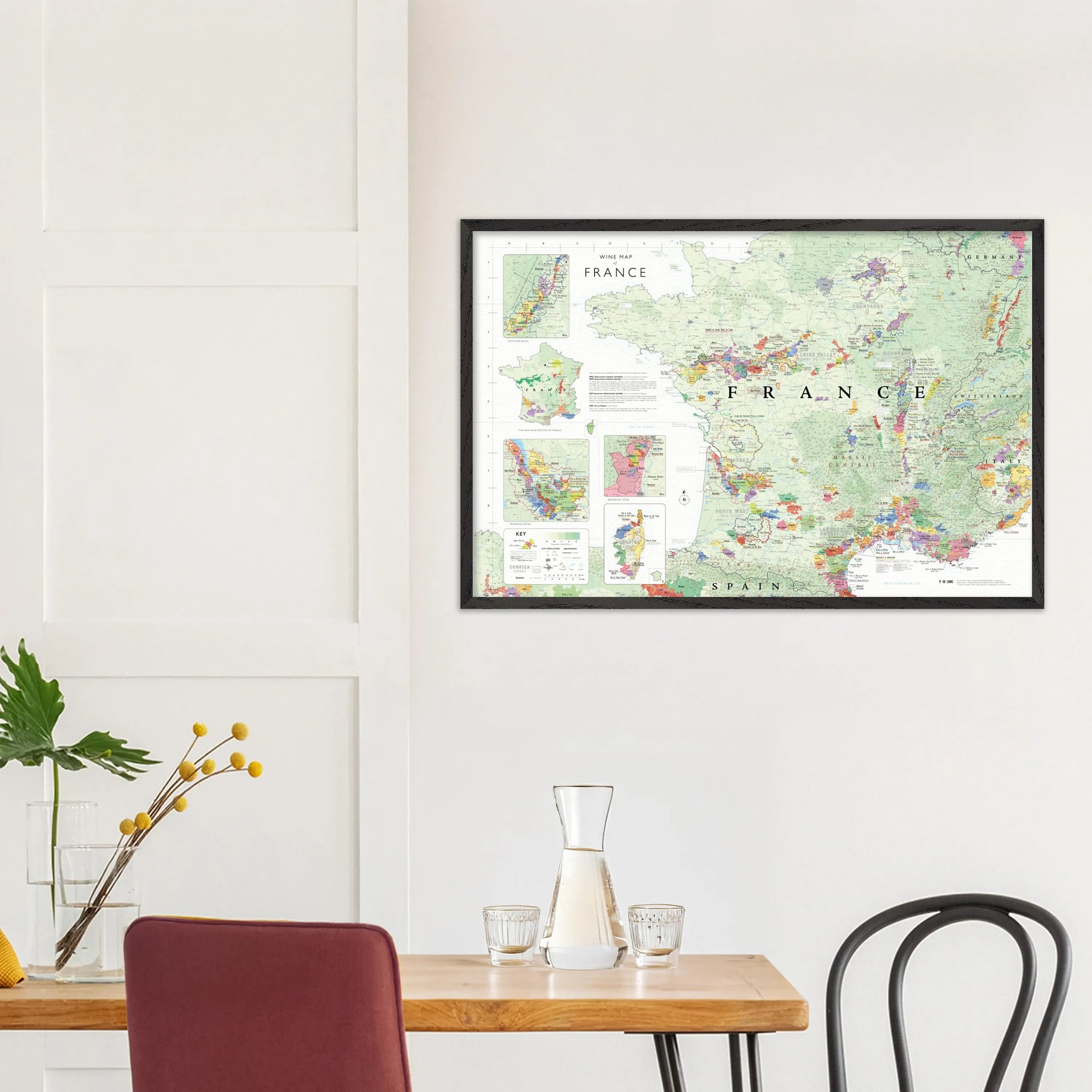 The De Long Wine Map of France Framed hangs above a dining table set with chairs, a vase, and glassware.