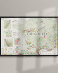 The Wine Map of France Framed features colored and labeled wine regions, highlighting detailed geography. Displayed in a wood frame, it hangs on a light-colored wall with gentle shadows creating an elegant effect.