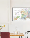 The De Long Wine Map of France IGPs Framed hangs on a white wall above a minimalist dining table.