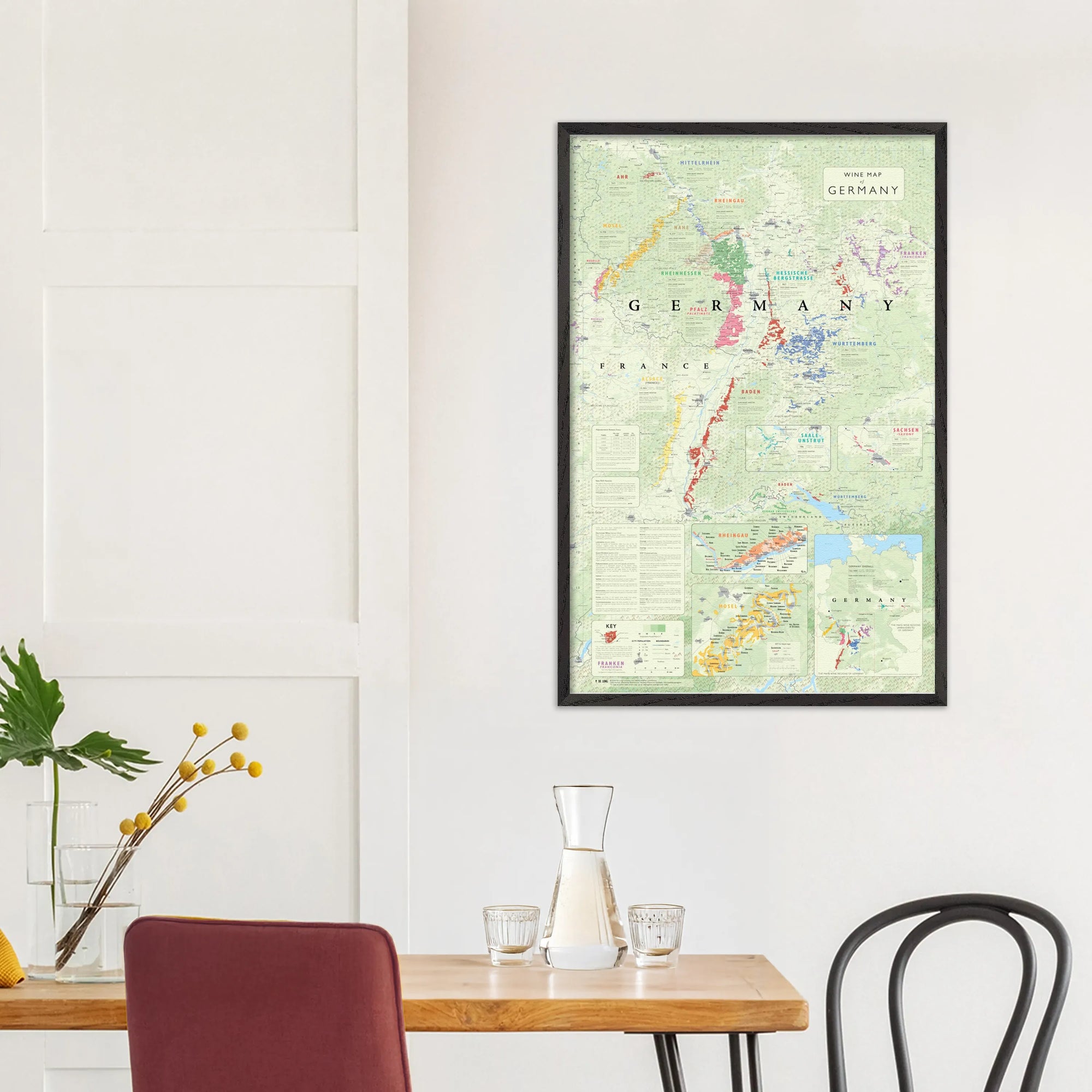 The De Long Wine Map of Germany Framed hangs on a white wall above a dining table with yellow flowers.
