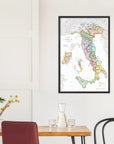 A De Long Wine Map of Italy IGTs Framed hangs on a white wall above a dining table with chairs and a glass carafe.