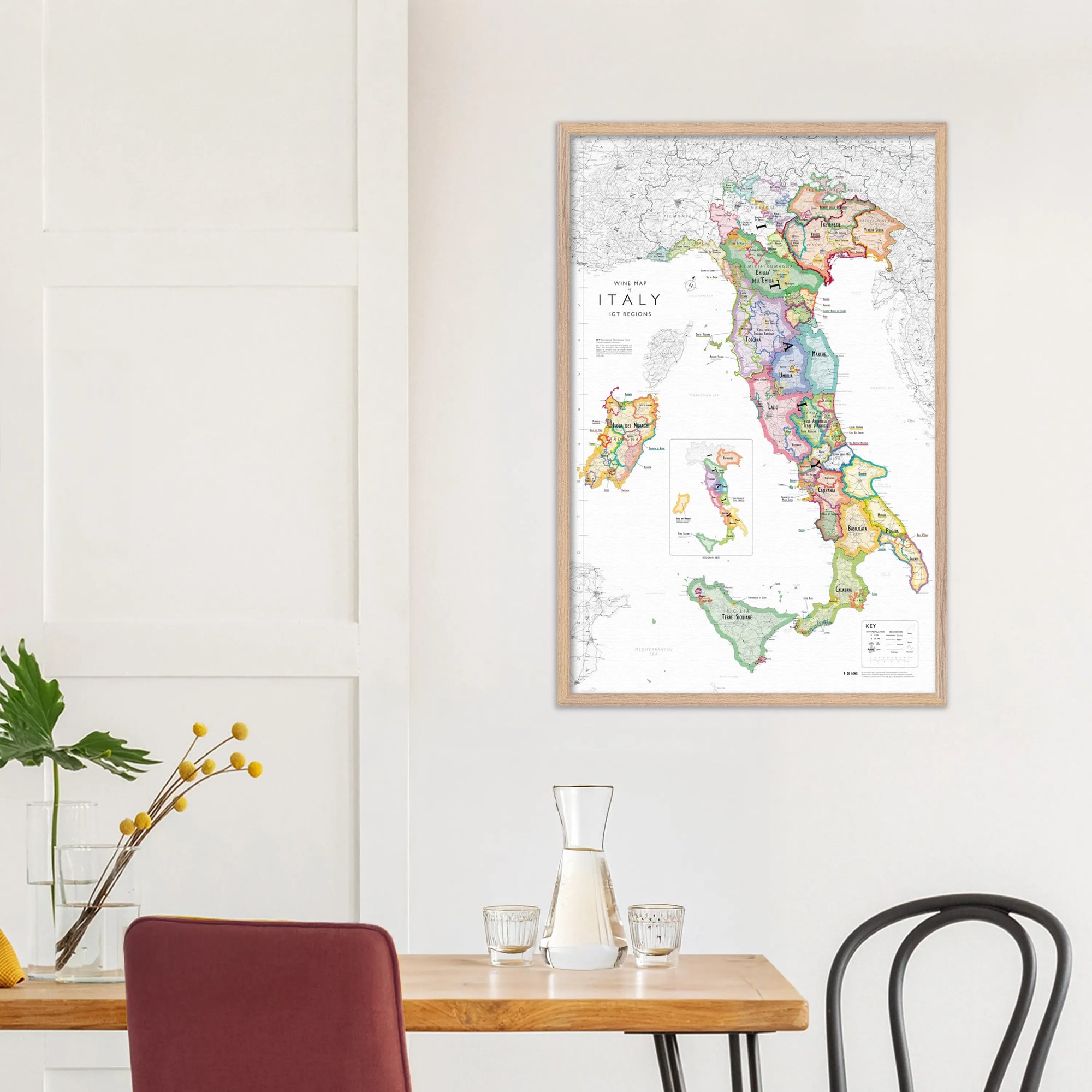 A De Long Wine Map of Italy IGTs Framed hangs on a white wall above a small dining table with minimalist decor.