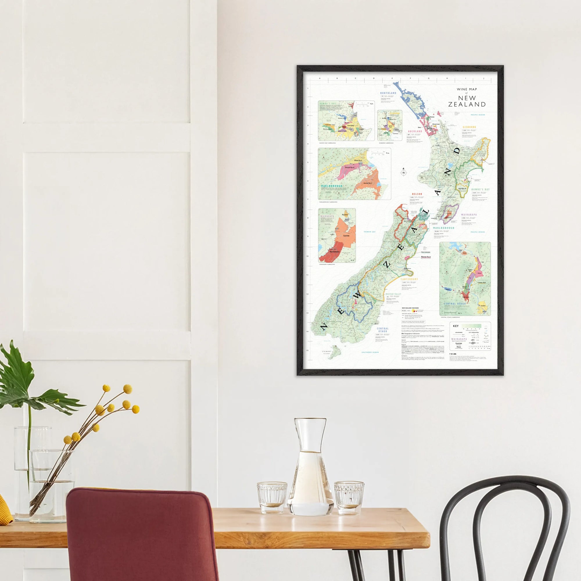 A De Long Wine Map of New Zealand Framed hangs above a table set with glassware and yellow flowers.