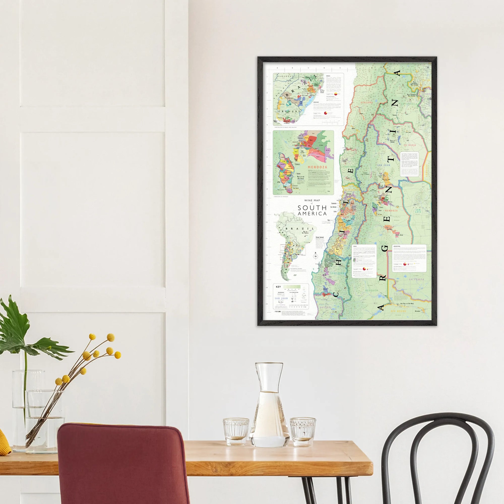 De Long's Wine Map of South America Framed displayed above a dining table with chairs, vase, and glassware.