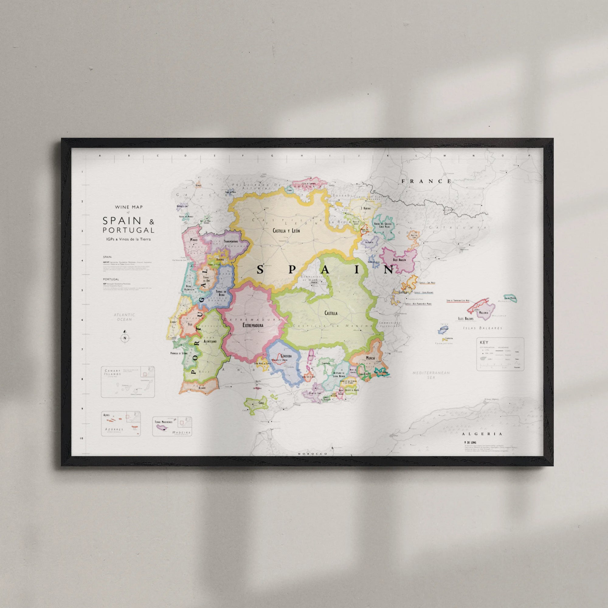 Wine Map of Spain & Portugal IGPs Framed, featuring vividly outlined regions. Sunlight casts gentle shadows on the colorful map as it hangs on a light wall.