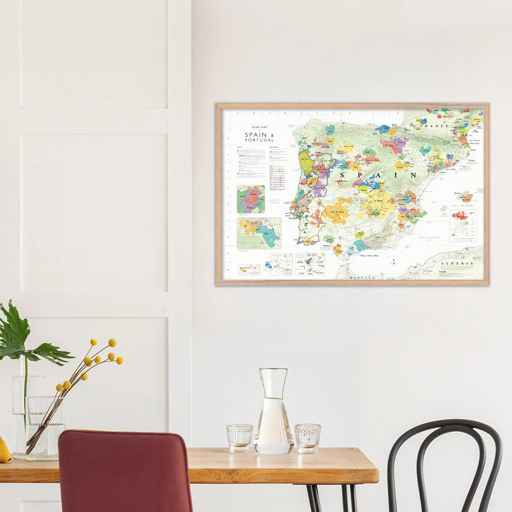 A De Long Wine Map of Spain &amp; Portugal Framed hangs above a small dining table with chairs and a plant.