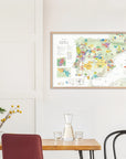 A De Long Wine Map of Spain & Portugal Framed hangs above a small dining table with chairs and a plant.
