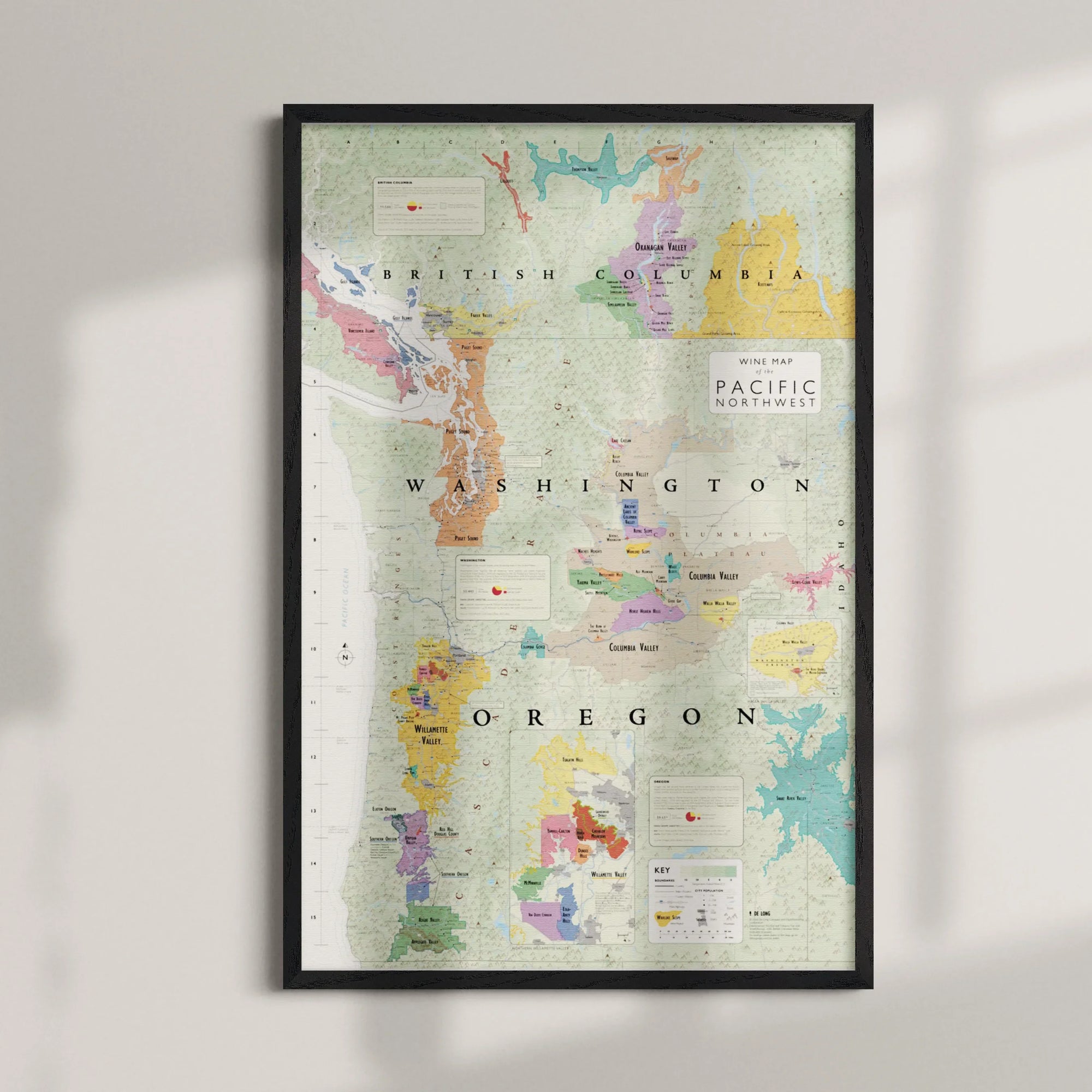 The Wine Map of the Pacific Northwest Framed is displayed on a wall, featuring Oregon, Washington, and part of British Columbia with colorful regional markings and text labels.