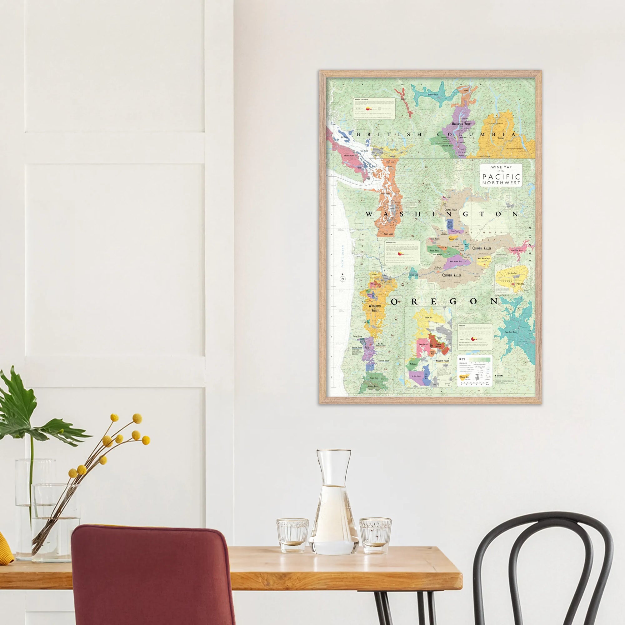 A De Long Wine Map of the Pacific Northwest Framed hangs above a modern dining table on a crisp white wall.