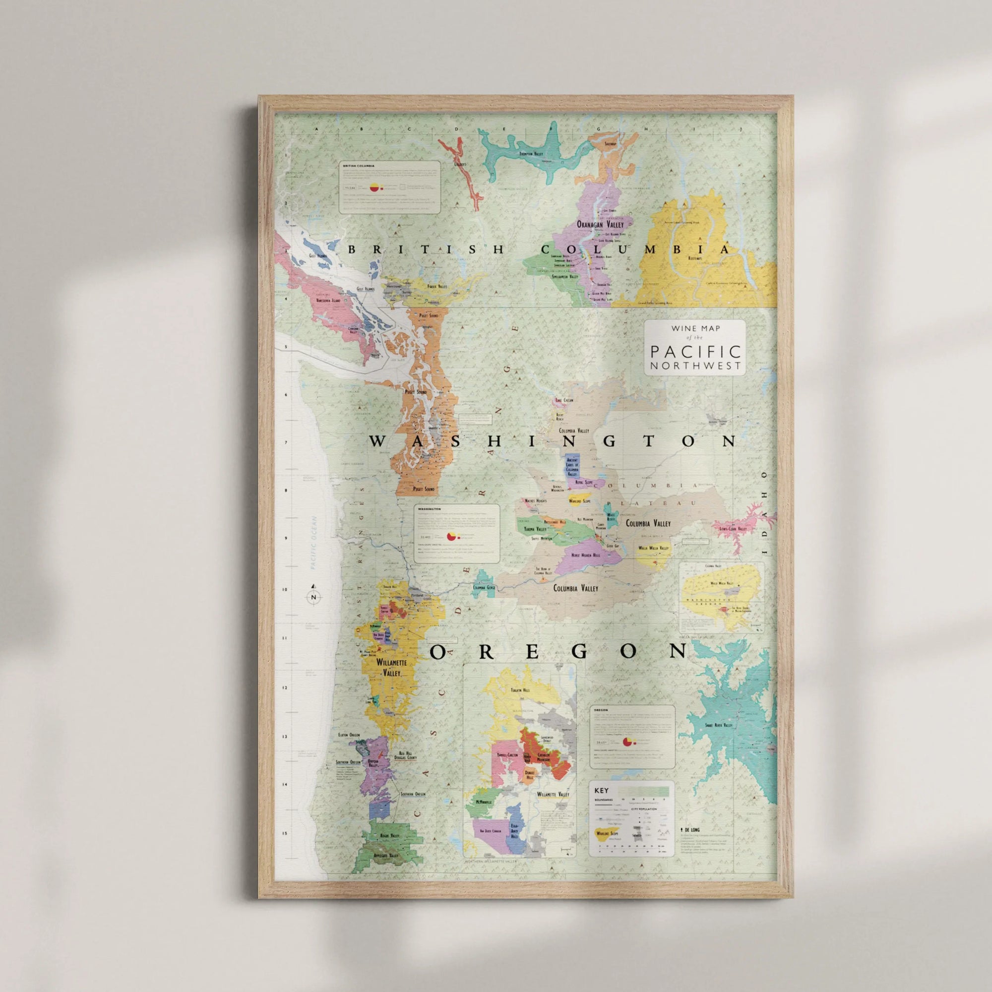 The Wine Map of the Pacific Northwest Framed features colorful sections and labels for Oregon and Washington wine regions, displayed on a light wall with soft shadows and a wood frame.