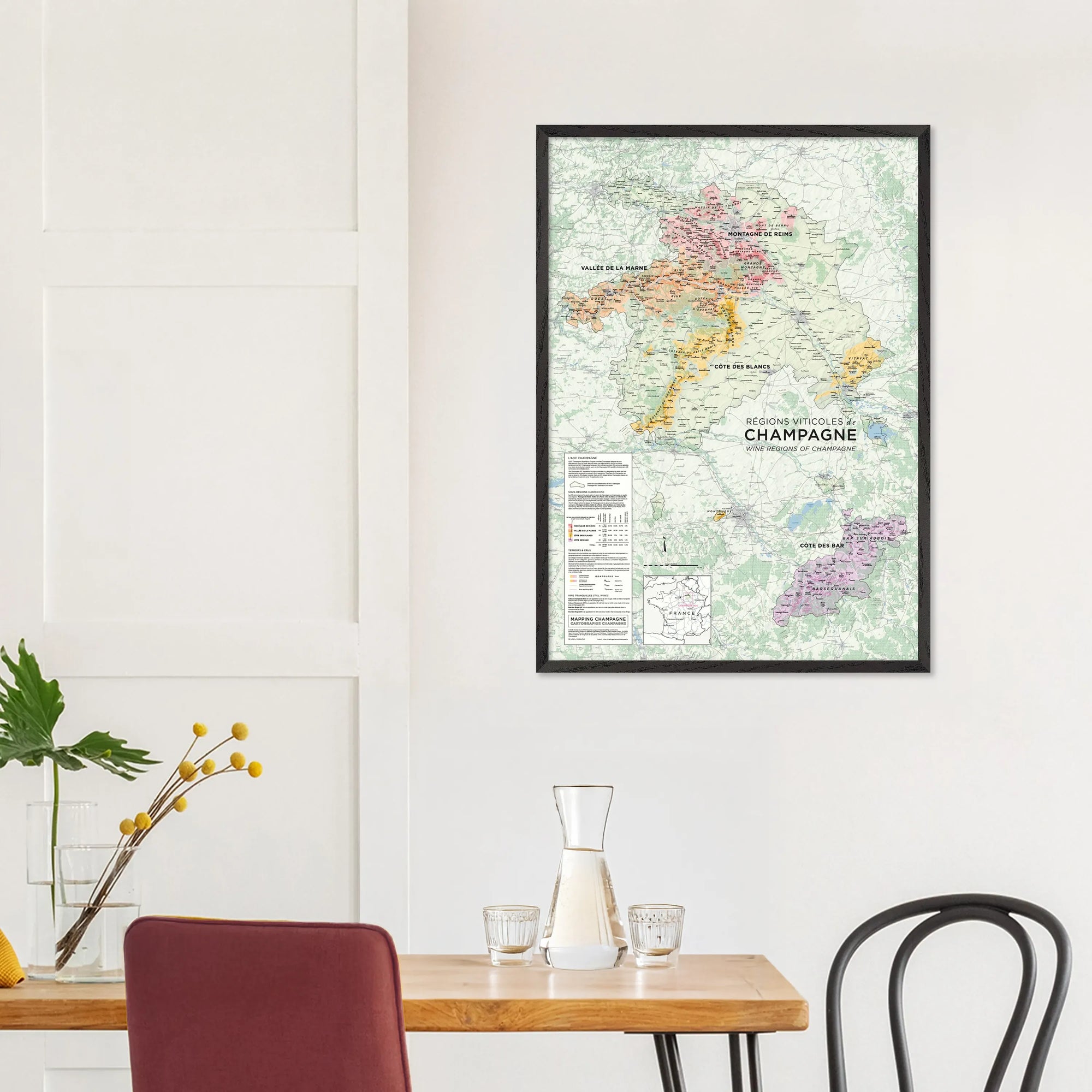 A De Long Wine Regions of Champagne Framed map (A1, wood frame) hangs above a dining table with chairs and a carafe.