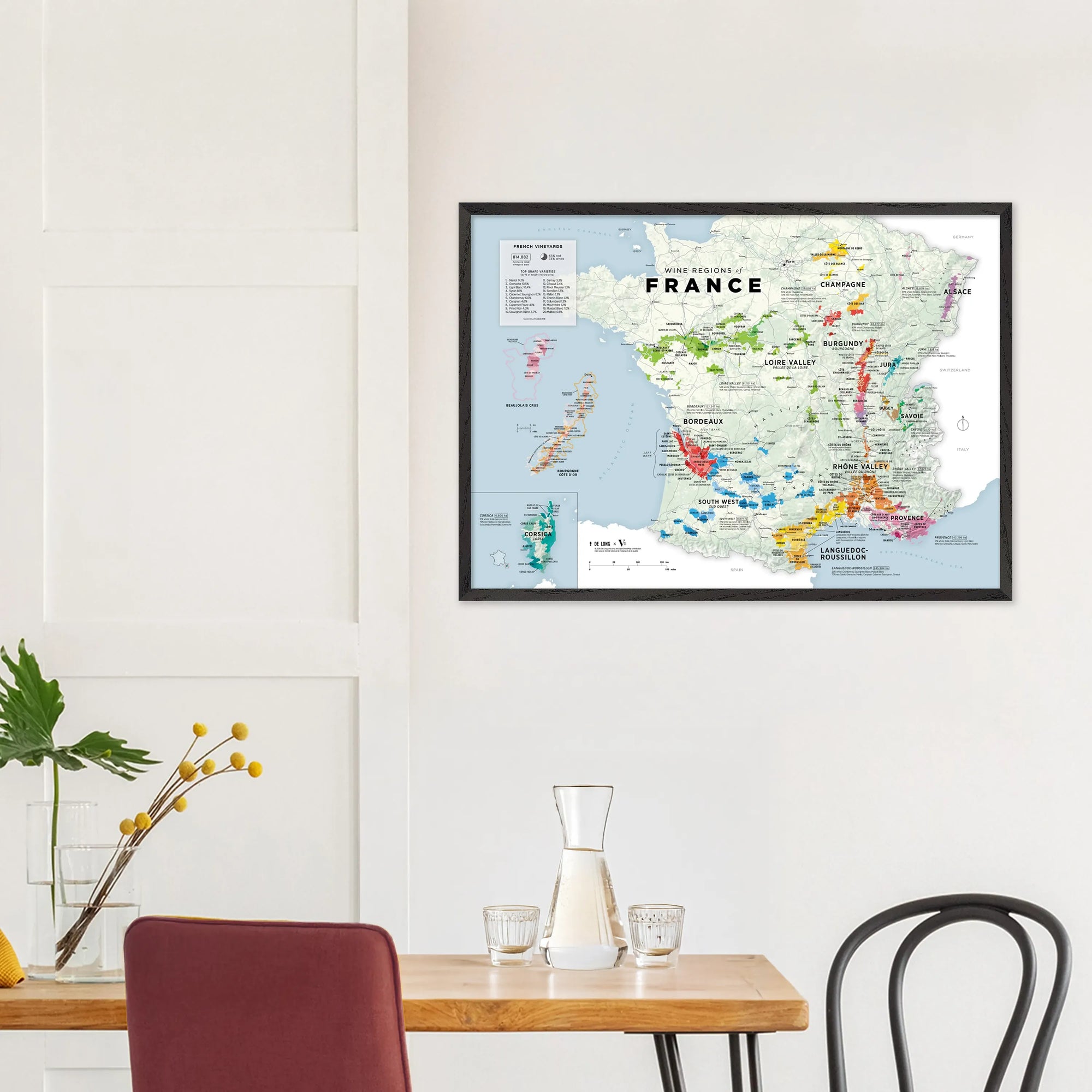 A De Long Wine Regions of France Vino One Framed map hangs above a dining table set with glassware and a plant.