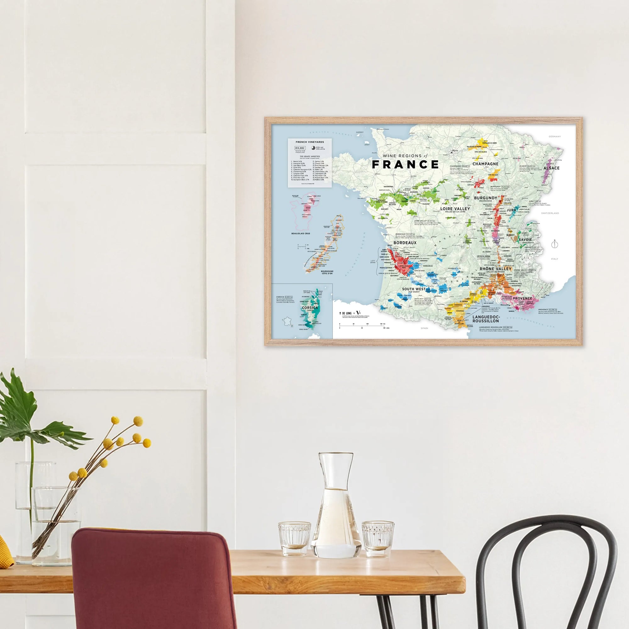 Wine Regions of France Vino One Framed by De Long displayed on a white wall above a dining table with carafe and plant.