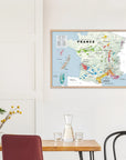 Wine Regions of France Vino One Framed by De Long displayed on a white wall above a dining table with carafe and plant.