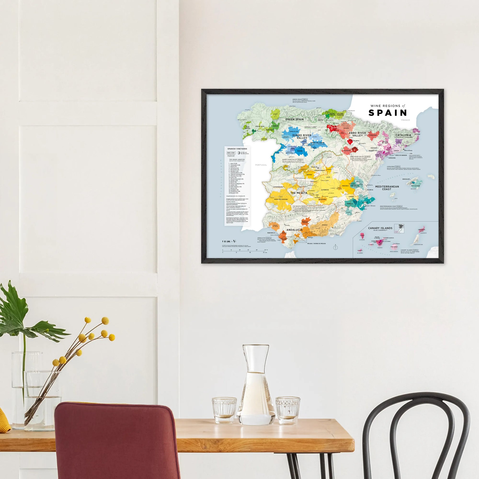 A De Long Wine Regions of Spain Vino One Framed print hangs above a minimal dining table with chairs.